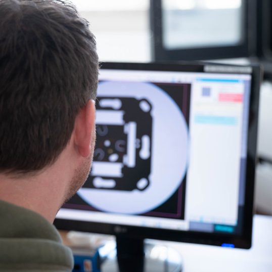 Symbolising the complete service. Christian Friedenstab out of focus in the foreground monitoring the component measurement in front of a CAD view.